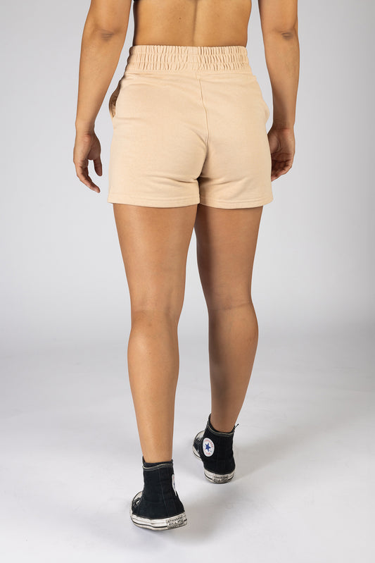 A woman posing against a light background in cream shorts.