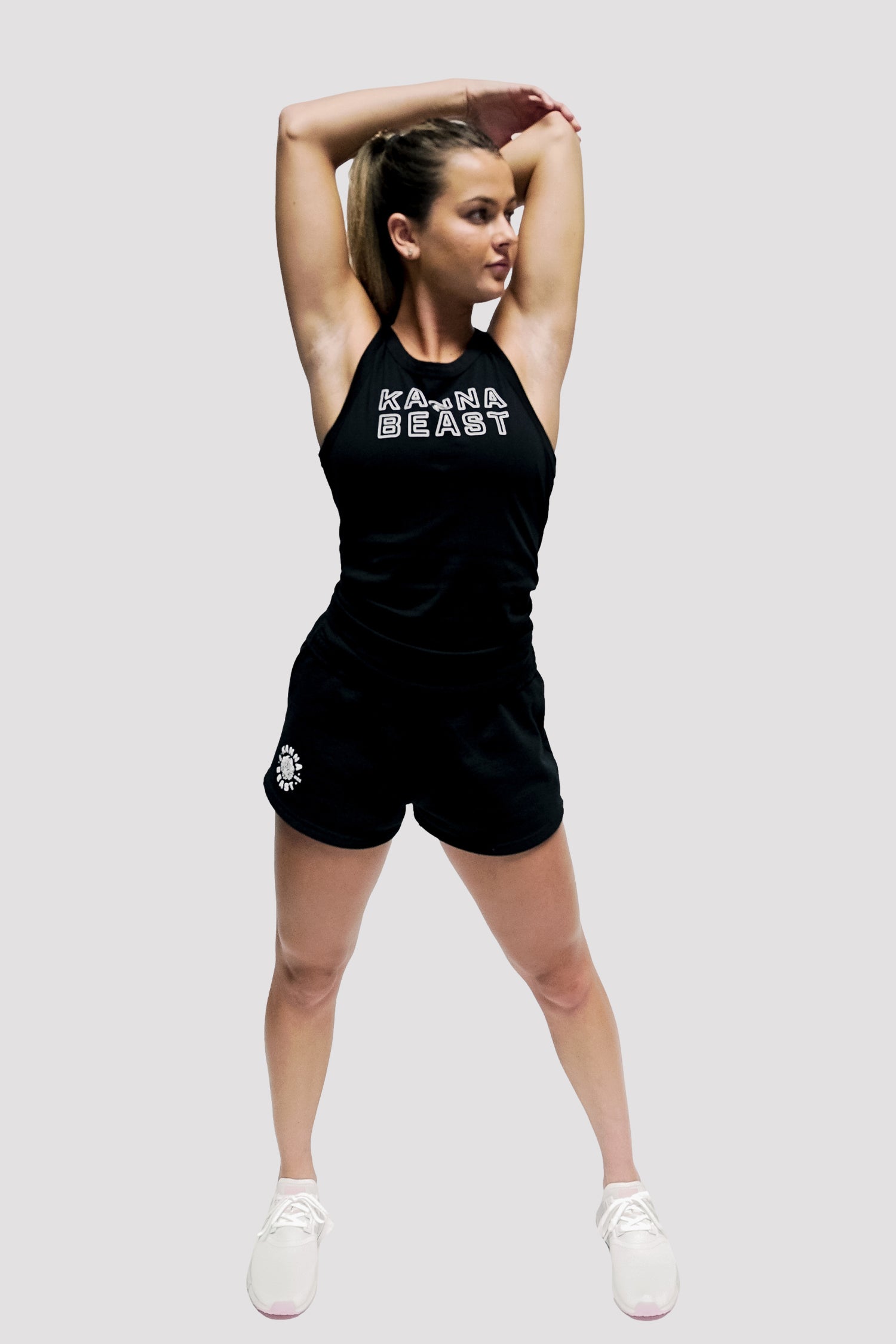 Model wearing Kanna Beast Tank Top posing with her arms above her head. Wearing black shorts and black tank top.
