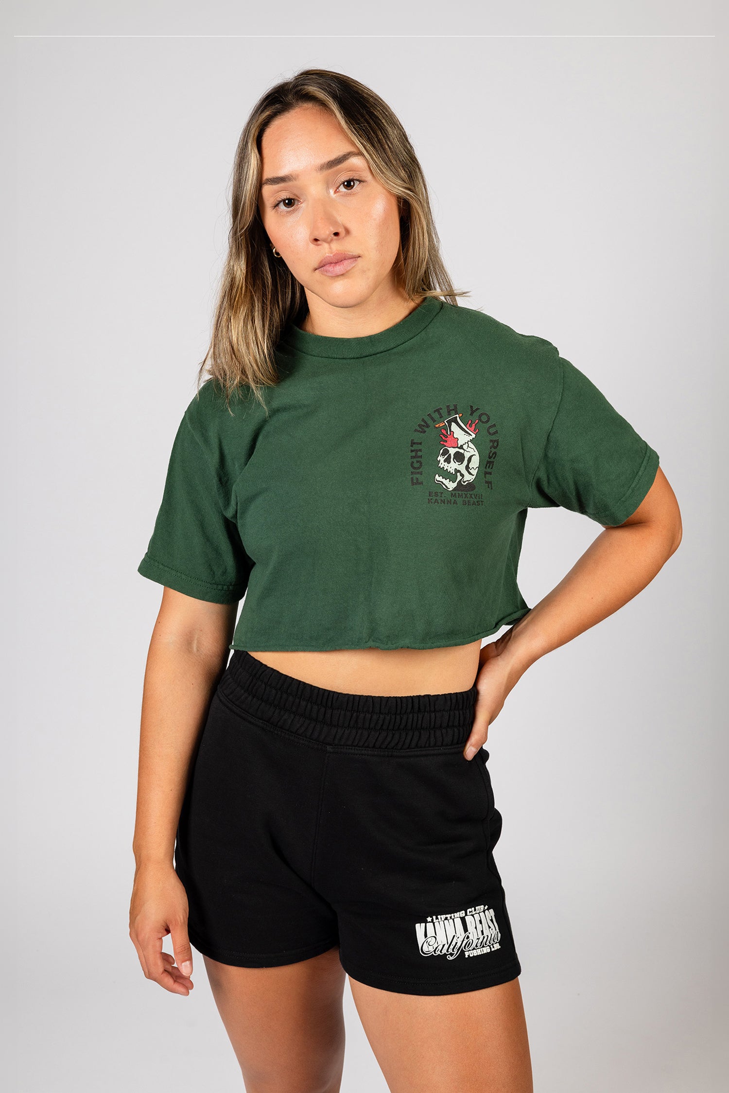 Female model with brown hair wearing a forest green crop-top t-shirt featuring a skull and the words 'Fight With Yourself'.