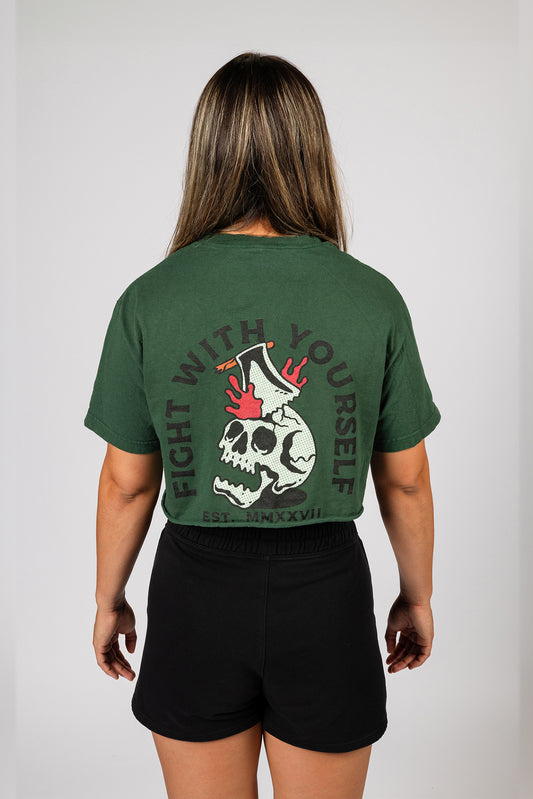 Female model showing the back of a forest green crop-top t-shirt featuring a large skull and the words 'Fight With Yourself'.