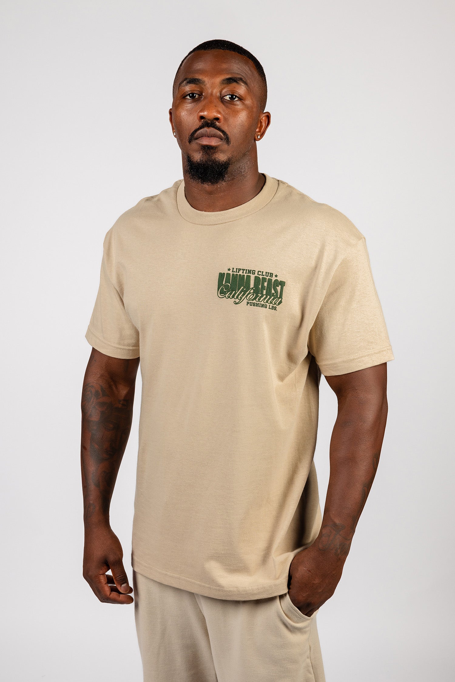 Male model wearing sand Kanna Beast graphic t-shirt featuring Kanna Beast logo and motto 'Lifting Club, Pushing LBs' in green on the left chest. 