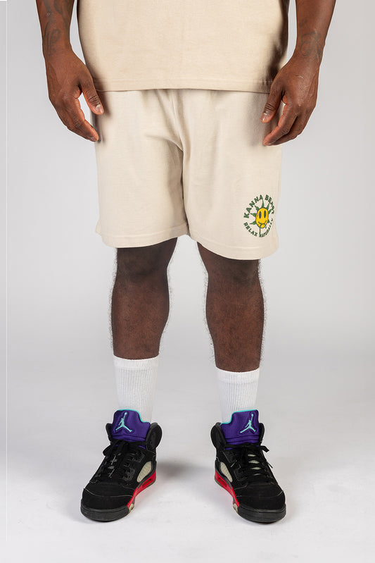 Man wearing sand athletic shorts with Kanna Beast Smiley Face graphic and text "Relax Naturally" paired with white socks and black sneakers