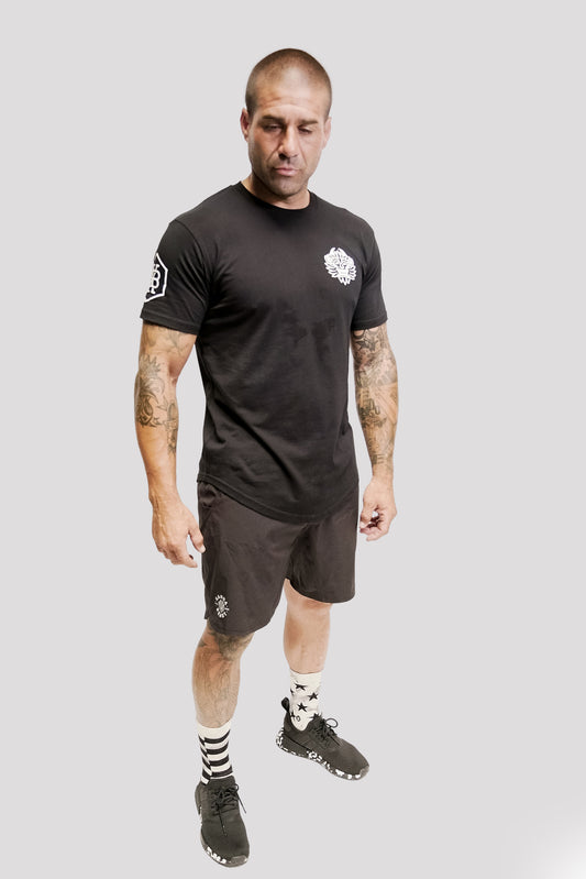 Male model wearing the Kanna Beast Tee and black shorts looking down and away from the camera. Our logo face on the front left chest and KB moniker on right shoulder. 