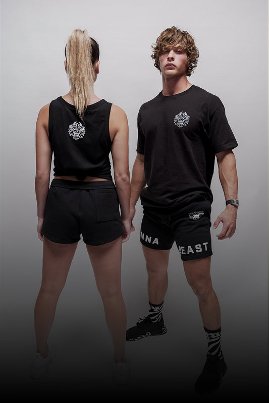 Two models, male and female,wearing all black Kanna Beast Essentials. Male model is wearing black t-shirt and shorts and female model is wearing black tank top and shorts. 